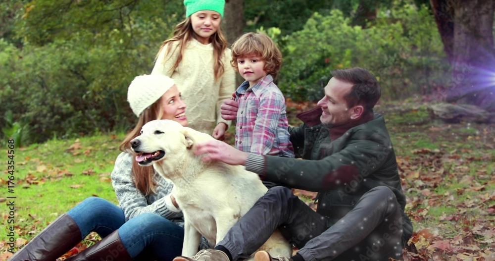 Fototapeta premium Sitting family of four holding and petting white dog at wooded park clearing, fallen leaves