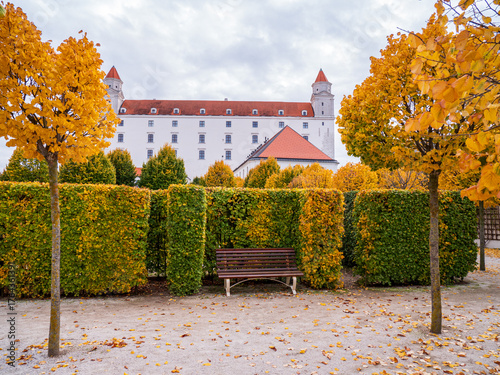 Canvas Print Bratislava Castle with autumn linden trees and trimmed hedges in a quiet baroque garden, with an empty bench creating a peaceful atmosphere