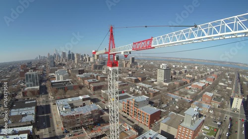 Crane boom over urban construction rooftop with city skyline and river view, construction crane towering over neighborhood