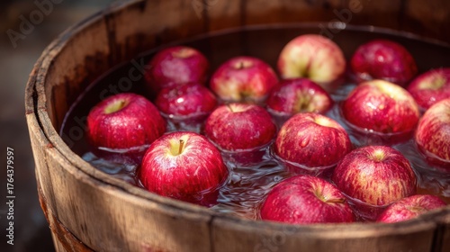 Bright red apples floating in a rustic wooden barrel filled with water. The apples are fresh, shiny, and vibrant, evoking a sense of harvest, autumn, and tradition