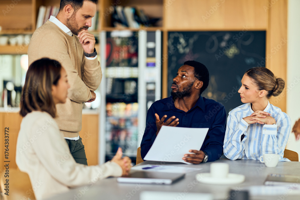 Fototapeta premium African-American Man Leads Discussion With Asian Woman and Colleagues in a Modern Office Meeting