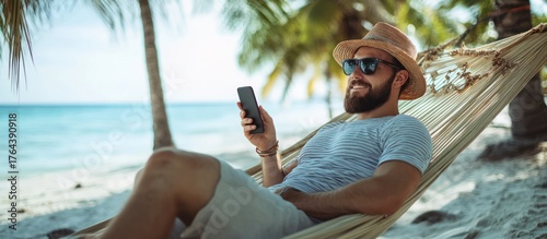 Relaxed man on a beach hammock, using a phone