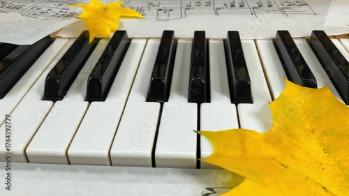 An Autumnal Melody in the Making: Close-up of piano keys adorned with handwritten musical scores and bright yellow maple leaves, capturing a moment of creative inspiration and the nostalgic beauty