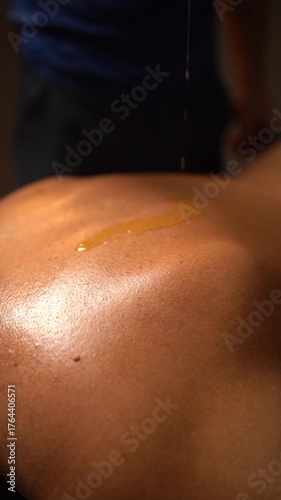 Close-up of a male therapist pouring warm massage oil onto a woman's back before a relaxing spa treatment.