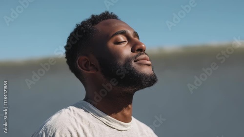 Wallpaper Mural Portrait of a serene young man standing outside, basking in sunlight with a gentle smile and closed eyes. The tranquil atmosphere highlights themes of mindfulness, wellness, and self care Torontodigital.ca