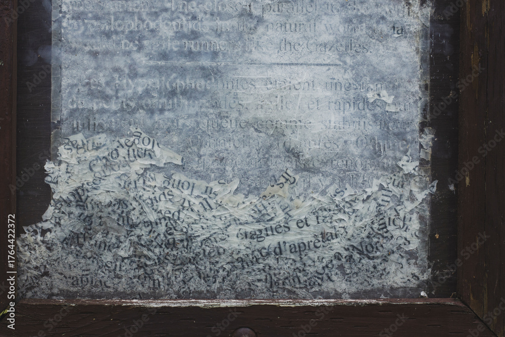 Obraz premium Close-up of weathered and partially erased text on a glass surface, framed by chipped dark wood. The faded black letters on a cloudy white background evoke age, decay, and forgotten information.