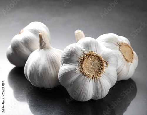Close-up shot of several heads of garlic on a shiny, dark surface, lit from the side