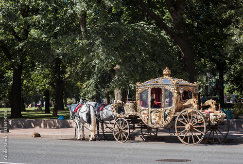 Foto A golden, royal carriage with white horses in the city park near St