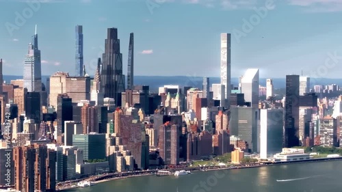 A 70mm cinematic drone shot over the East River, slowly moving from left to right along the coastline, capturing the Manhattan skyline and its towering skyscrapers, of New York City, NY.