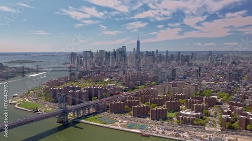 This aerial perspective emphasizes the contrast between the serene water of the East River and the bustling, vibrant urban environment of New York City, with the Williamsburg bridge connecting between