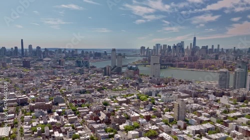 A cinematic aerial drone shot captured from the Brooklyn side, featuring the Williamsburg bridge crossing the East river into lower Manhattan, with the iconic Freedom tower, of New York City.