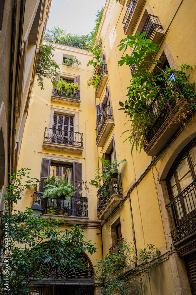 Fototapeta premium Tall yellow building courtyard with abundant greenery and balconies vertical