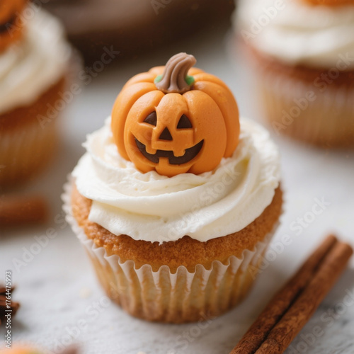 Close-up of pumpkin spice cupcake topped with creamy white frosting and fondant pumpkin autumn and Halloween dessert decoration