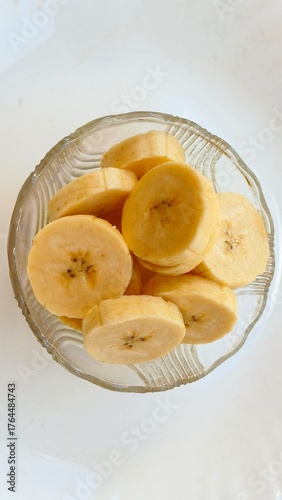 Closeup of organic ripe banana fruit cut piece slice in glass bowl served or isolated on white table background. Healthy eating, weight loss diet, wellness lifestyle and snack craving concept.