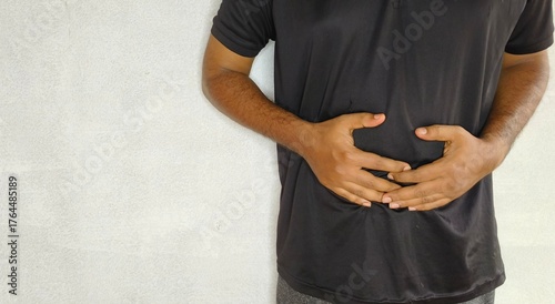 Young adult asian man with hand on stomach isolated on white background with copy space. Stomach ache, abdominal pain, diarrhea, food poisoning, upset belly, gas, cramp and appendicitis concept.