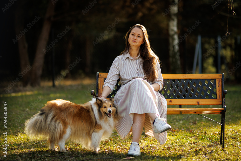 Naklejka premium Woman sitting on bench with fluffy sheltie dog in garden