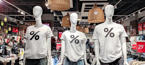 Mannequins in white t-shirts with percentage discount symbols in a retail clothing store.