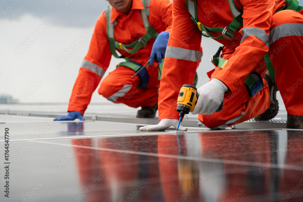 Fototapeta premium Two men in orange work clothes are fixing a solar panel