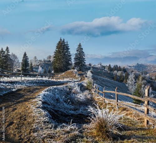 Winter coming. Last days of autumn, morning in mountain countryside peaceful picturesque hoarfrosted scene. Dirty road from hills to the village. Ukraine, Carpathian mountains.