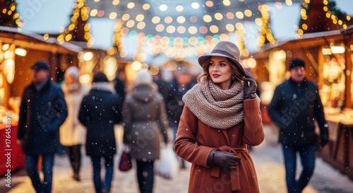 Woman walking through a festive street market with blurred lights and falling snow. Christmas season holiday celebration and winter atmosphere.