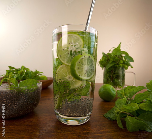 Glass of water with mint leaves, chia seeds and lemon slices on wooden table.