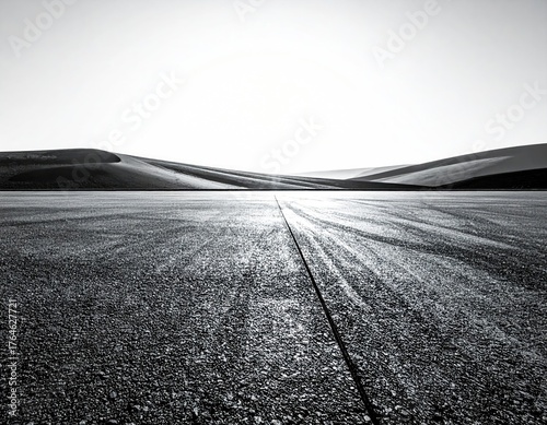 A black and white photo with a straight, paved road leading to rolling desert hills under a bright sky