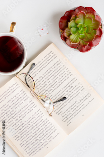 Close-up shot of revealing  book in English., top view. There are reading glasses on the book. A cup of tea and a cactus stand nearby. Pensioner's leisure