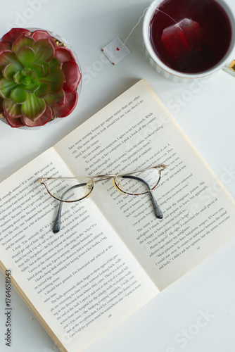 Close-up shot of revealing  book in English., top view. There are reading glasses on the book. A cup of tea and a cactus stand nearby. Pensioner's leisure