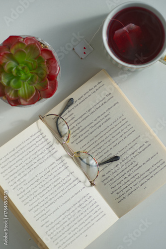 Close-up shot of revealing  book in English., top view. There are reading glasses on the book. A cup of tea and a cactus stand nearby. Pensioner's leisure