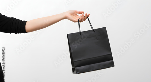retail and black friday sale concept - female hand holding black shopping bags on white background
