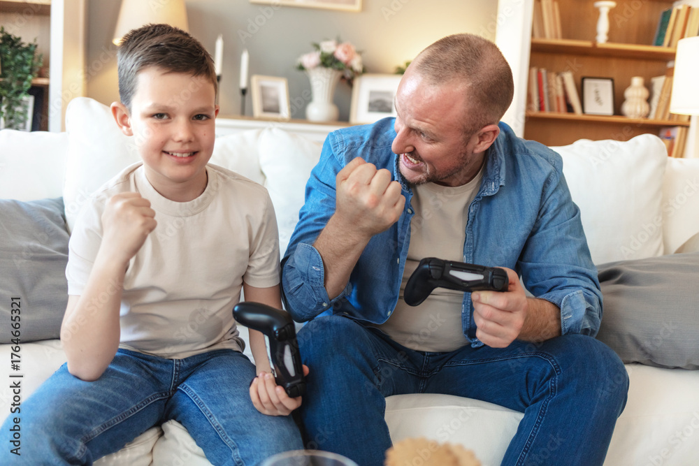 Obraz premium Father, child and win video game with celebration, competition and parent with son in home. Happy kid, dad and success with console with fist pump, victory and bonding together with family in lounge.