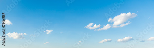 Wide panoramic clear blue sky background with a few white clouds. Bright sunny day with vast empty space.