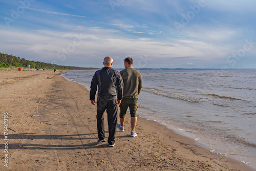 Rear view of father and son strolling along sandy shoreline, quiet conversation and generational bond in soft light