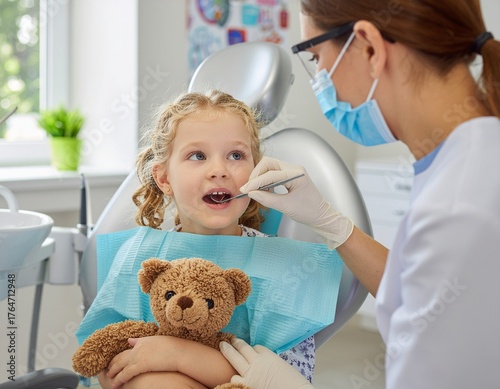 Dentist examining a 5-year-old child holding teddy bear in modern dental clinic