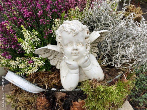 Engel auf dem Friedhof zwischen Blumen im Herbst mit Heidekraut im Blumentopf