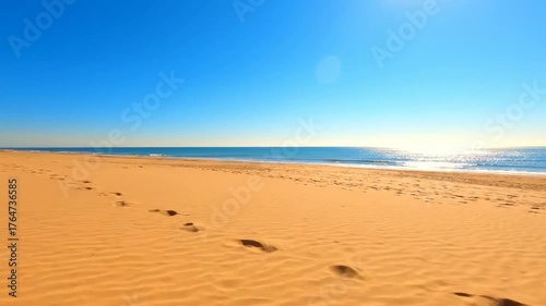 Footprints in the Sand: Footprints trace a path across the golden sand, leading towards the sparkling ocean under a brilliant blue sky, evoking a sense of journey and tranquility.