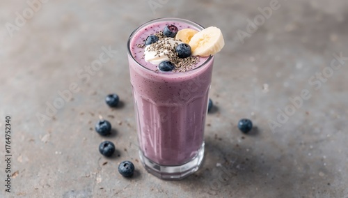 Glass of yogurt smoothie with banana, blueberries, and chia seeds on a gray concrete surface. Nutritious snack