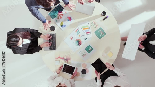 Aerial perspective of coworkers using tablets and charts during creative strategy discussion. Concept of teamwork, innovation, digital workflow, and confident focus in business planning.