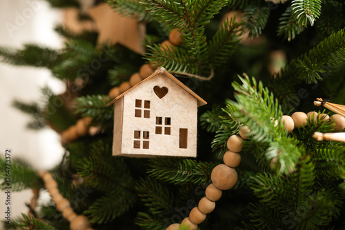 A charming wooden miniature house ornament hangs on a Christmas tree