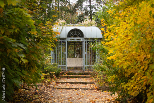 A secluded metal gazebo at the end of a winding path, surrounded by vibrant autumn foliage.