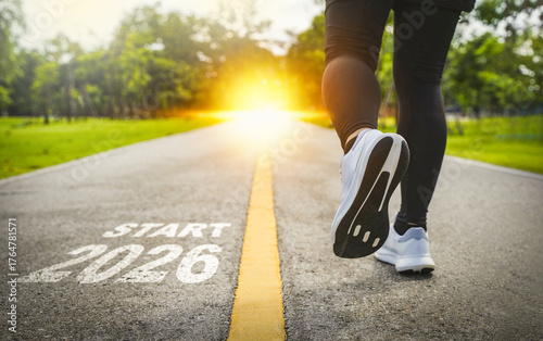 New Year 2026 concept. The beginning of success. The text 2026 is written on a paved road and a female runner is starting a new year. Concept of challenges or career paths and changes coming year.