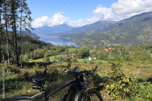 Electric mountain bike overlooking a lake surrounded by green hills and small villages. Scenic view of nature and mountains on a sunny day.