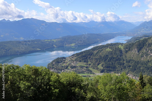 Panoramic view of Millstatter See surrounded by green hills and mountains. Beautiful alpine landscape under a clear blue sky.