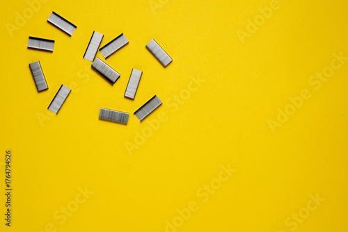 A top-down view of several strips of metal staples scattered in the top-left corner of a bright yellow textured background.