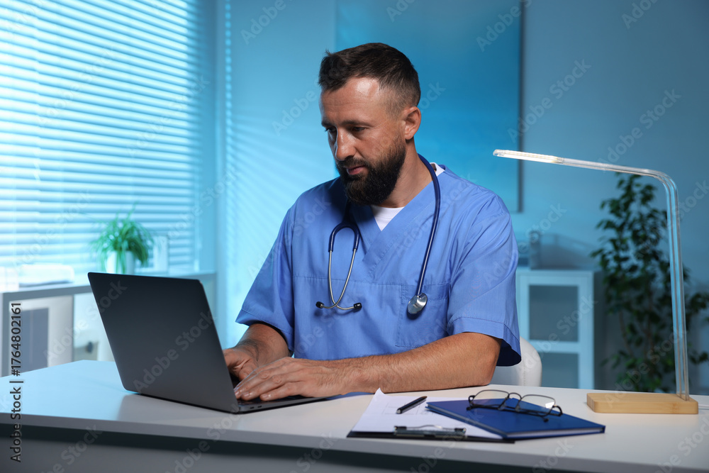 Fototapeta premium Doctor working on laptop at table in clinic during night shift