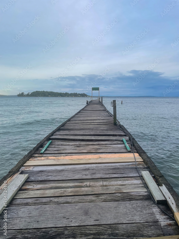 Fototapeta premium A weathered wooden pier stretches into the calm Caribbean Sea near Bocas del Toro, Panama. Cloudy blue sky