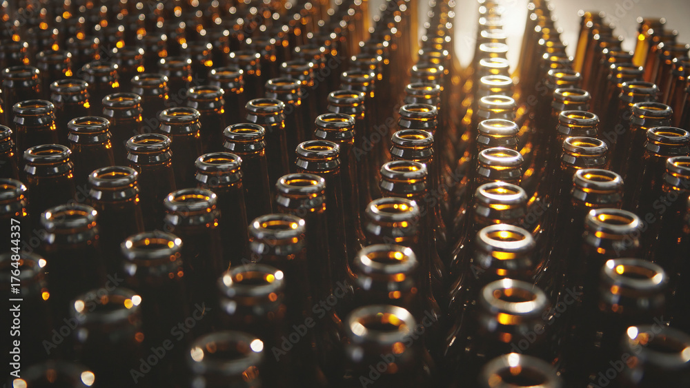 Fototapeta premium Brown glass bottles are processing on filling machine conveyors in a manufacturing plant, showing the repetition and mass production of beverages in a modern factory setting