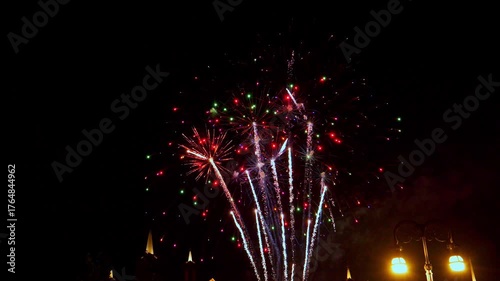 Bright fireworks explode in a variety of colors above the city skyline, creating a stunning visual performance against the dark night sky. The celebration fills the air with excitement.