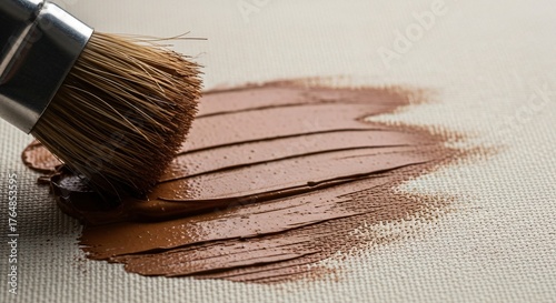 Close-up of a paintbrush applying brown paint onto a textured canvas surface.
