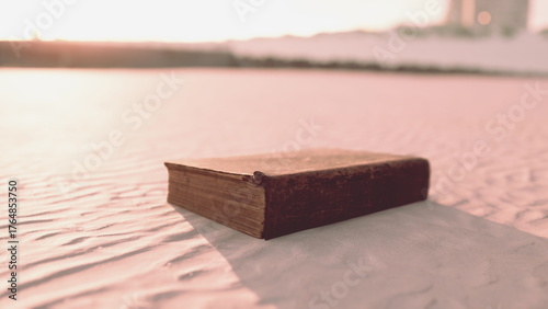 A weathered book lies open on soft, golden sand dunes, bathed in the warm glow of a vibrant sunset. The fading light enhances the allure of the setting, sparking curiosity.